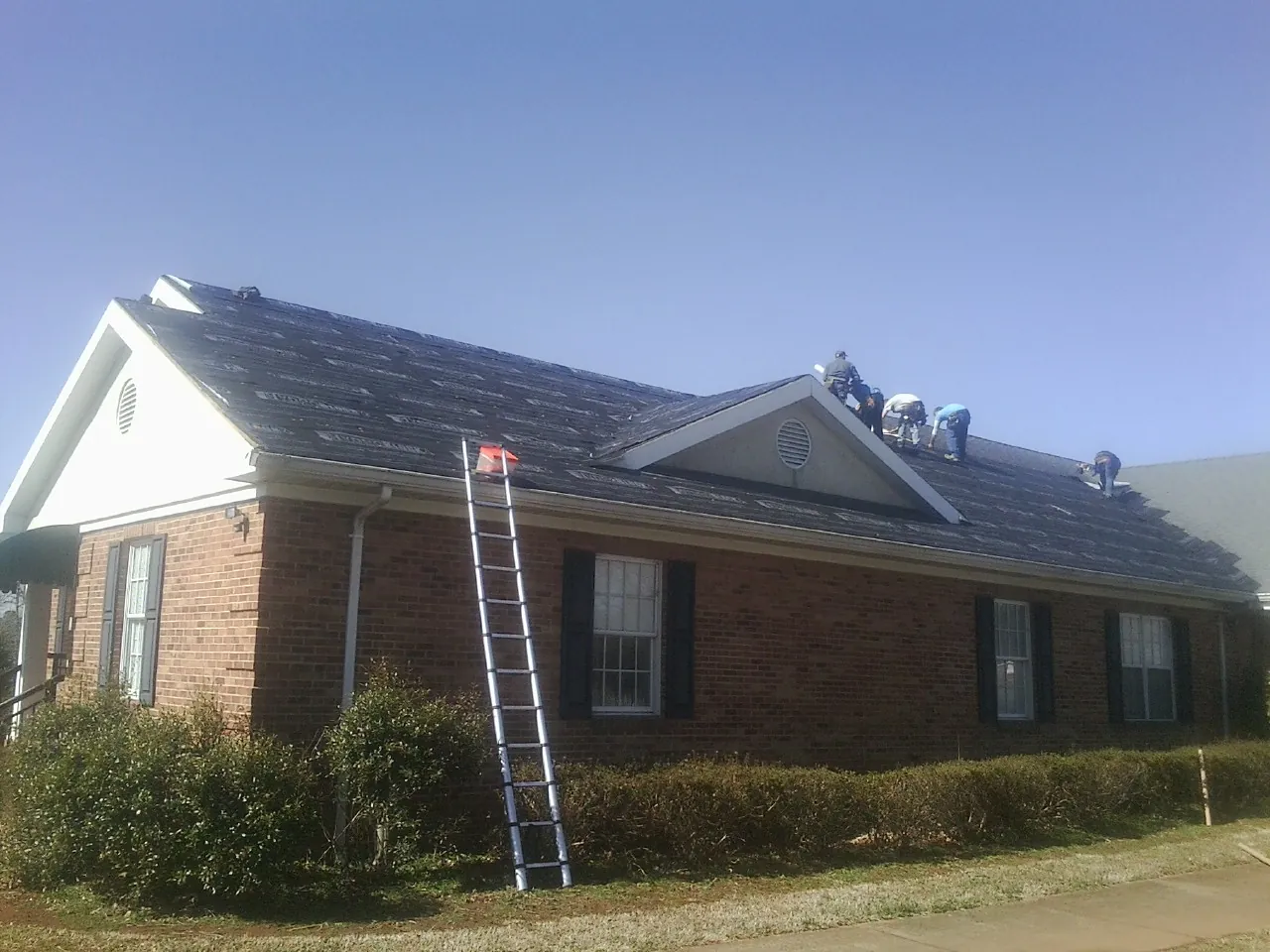 Crew tearing shingles off a brick ranch roof with a ladder set — Metal Roof Repair work by our crew in Stanwood