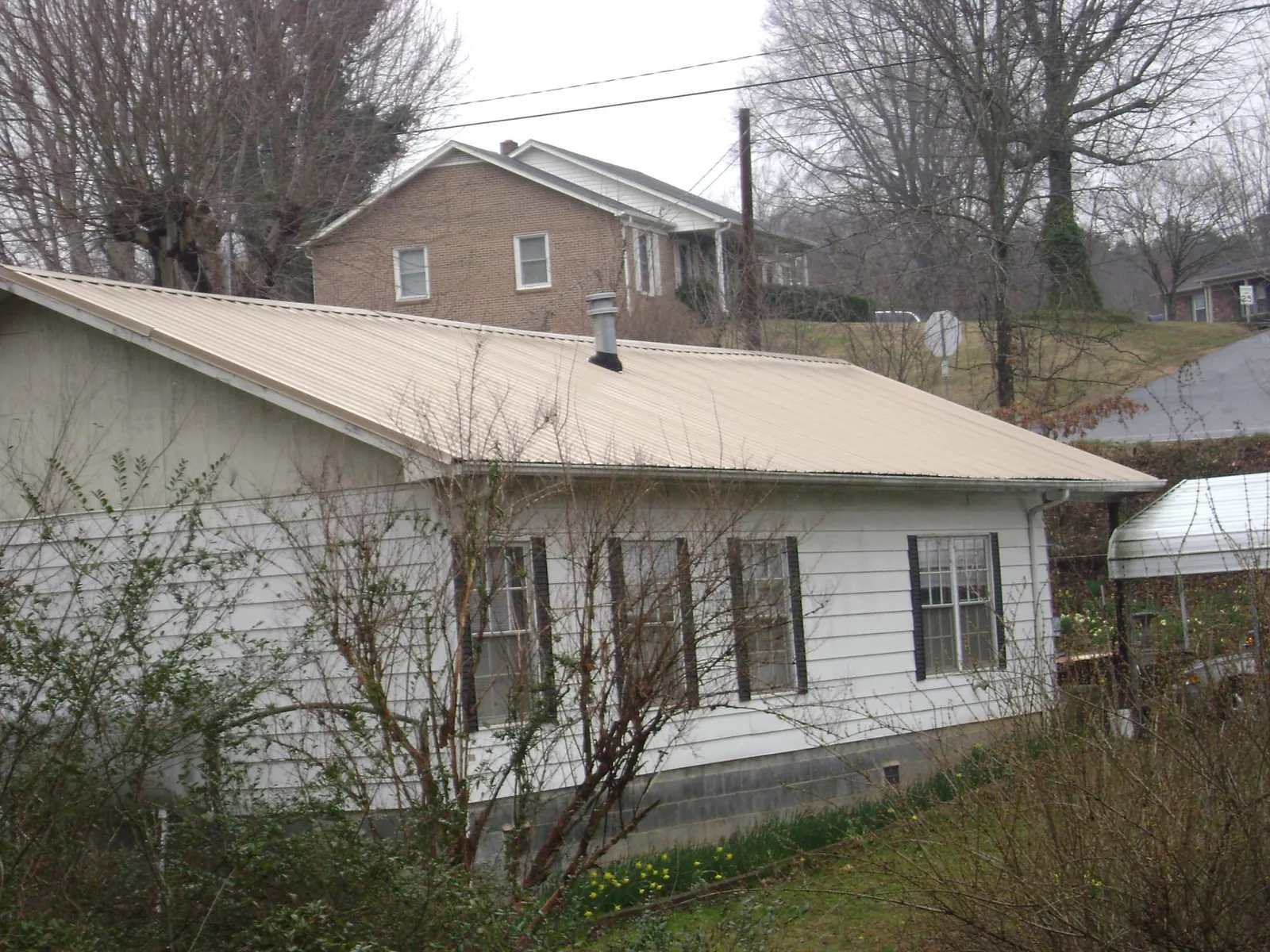 Tan metal roof on a white sided house set into a hillside — Commercial Roofing by Roofing Brothers in Stanwood